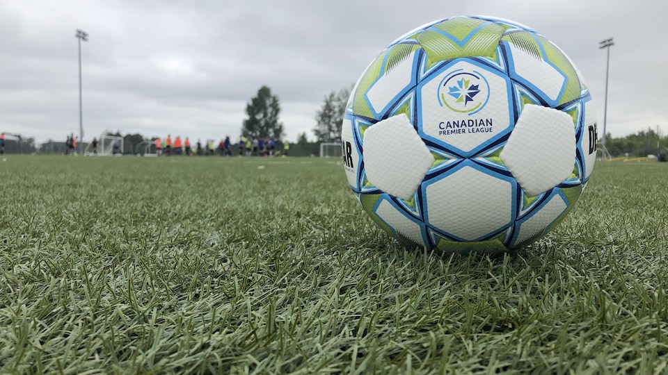 Un ballon aux couleurs et marqué du logo de la Première Ligue canadienne de soccer est posé sur le gazon artificiel d'un terrain.