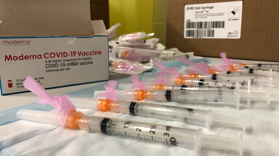 Des seringues de vaccin Moderna posées sur une table avec la boîte.