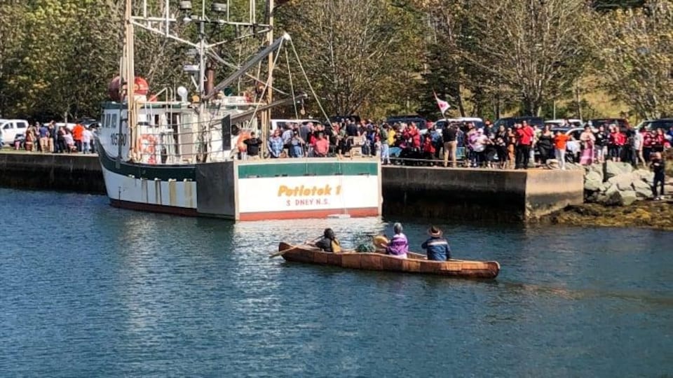 Un bateau de pêche est accosté à un quai, entouré de gens.