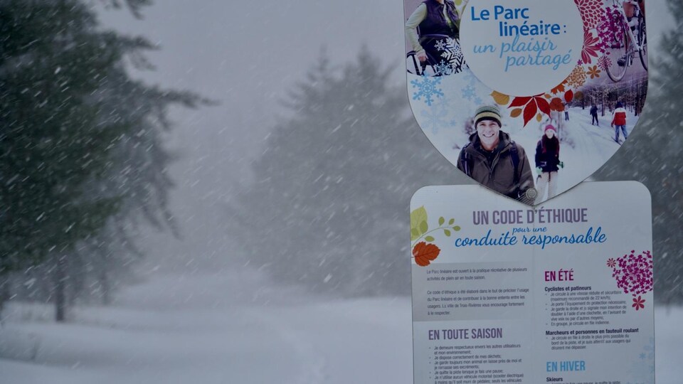 Pancarte du Parc linéaire et quelques sapins et traces de pas sous la neige                              