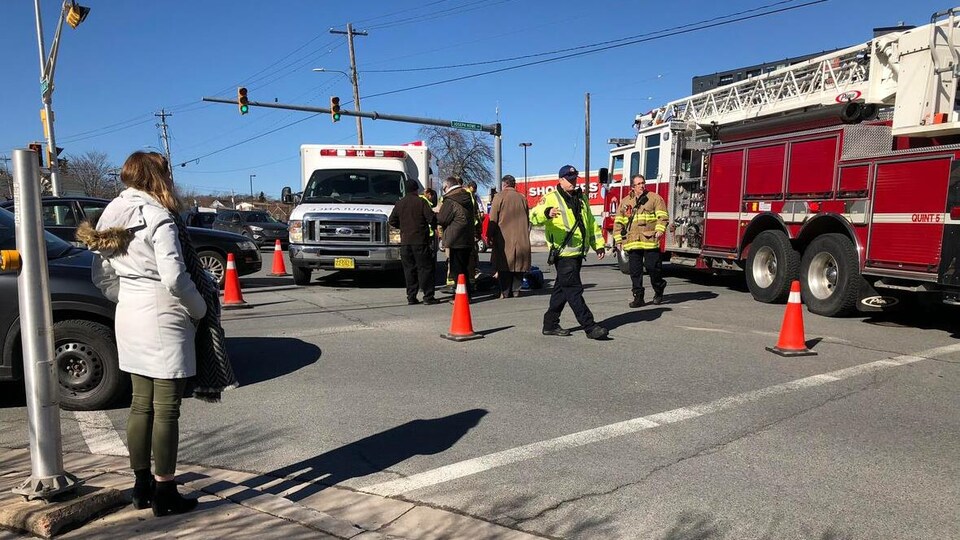 Une femme sur le trottoir observe un camion de pompier et une ambulance au milieu d'une rue.