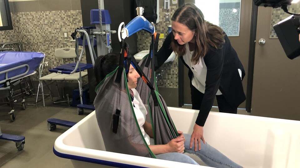 Une femme aide une autre femme à sortir d'une baignoire en utilisant un lève-personne.
