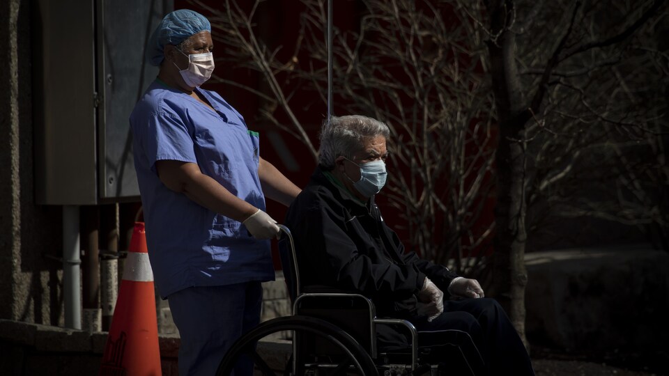 Une préposée avec un patient en fauteuil roulant, tous deux portant un masque.