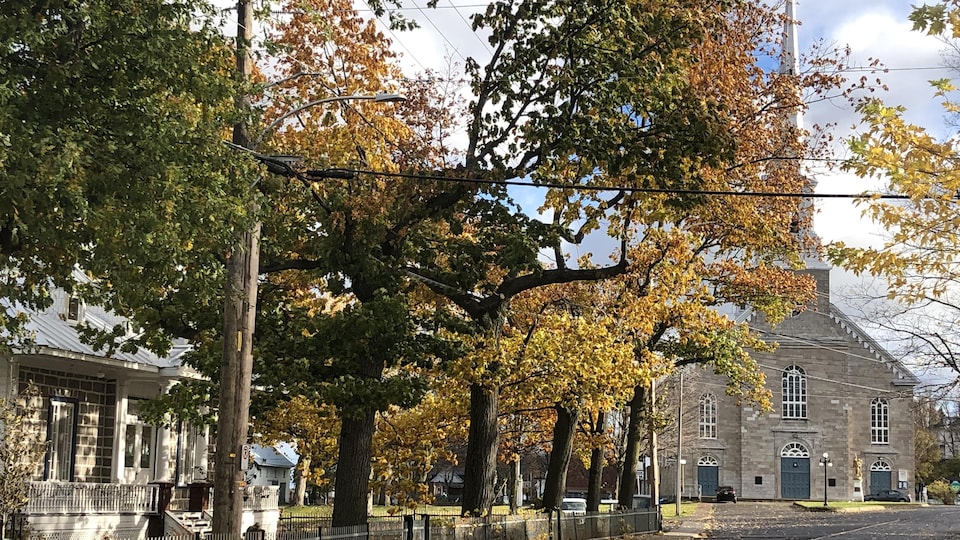Plan large d'une église dans un village, avec des feuilles aux couleurs d'automne dans les arbres.