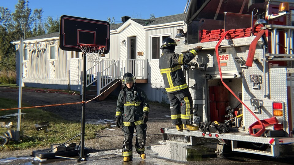 Deux pompiers dans l'entrée d'une maison avec leur camion.