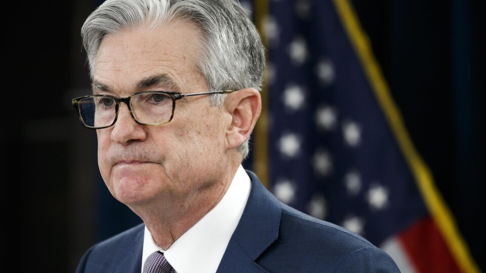 Jerome Powell l'air sérieux devant un drapeau américain.