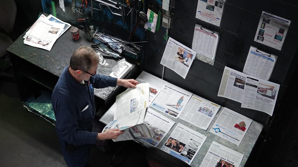 Michel Richard compare un exemplaire du journal avec les pages étendues sur une table.                             