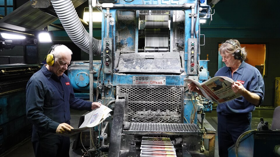 Deux pressiers regardent le journal devant une machine. 