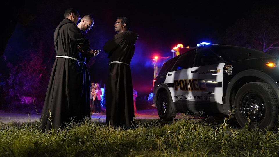 Des prêtres discutent près d'un véhicule de police.
