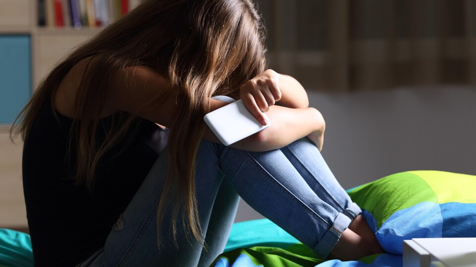 Une adolescente, un téléphone intelligent à la main, assise sur un lit