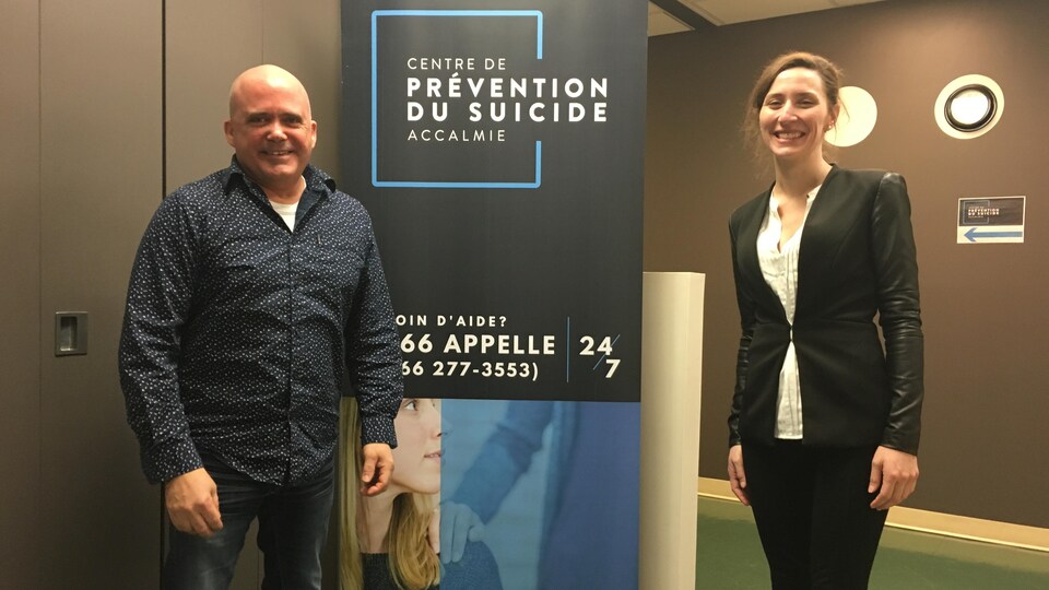 Deux personnes posent près d'une affiche