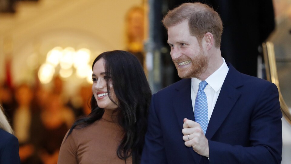 Le prince Harry et Meghan Markle sortent d'un bâtiment en se tenant par la main et en souriant.