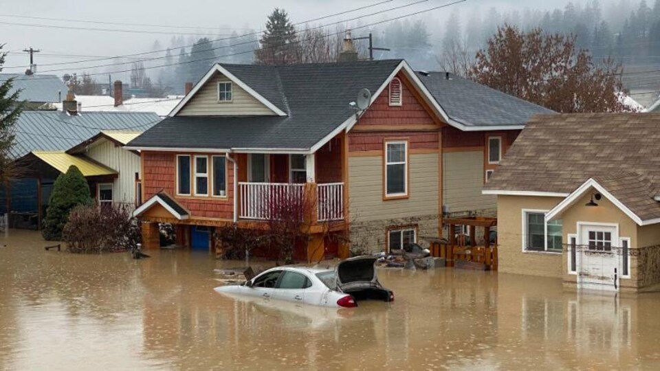Une voiture immergée dans de l'eau devant des maisons elles aussi inondées.