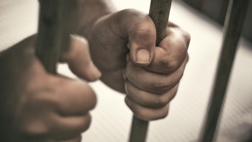 Un homme tient les barreaux d'une cellule de prison.