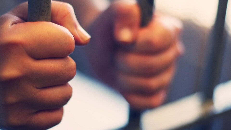 Un homme tient les barreaux d'une cellule de prison.