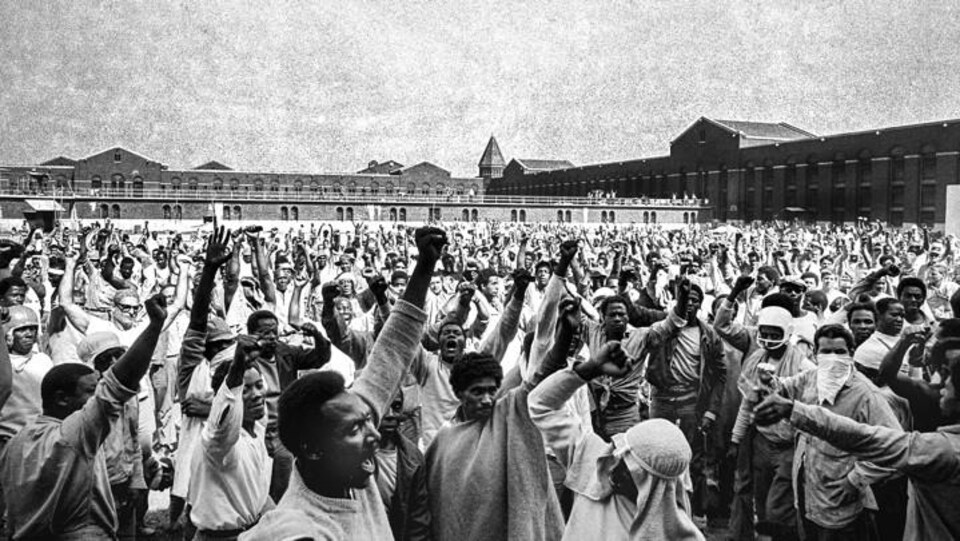 Plusieurs prisonniers lèvent le poing dans une cours de prison.