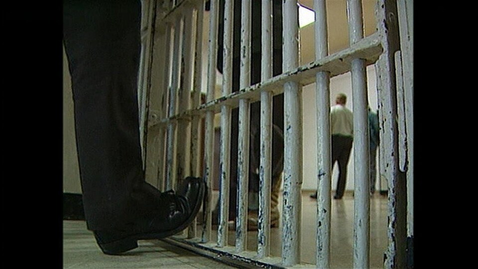 Des barreaux séparent les jambes de deux personnes qui se font face à l'intérieur d'une prison.