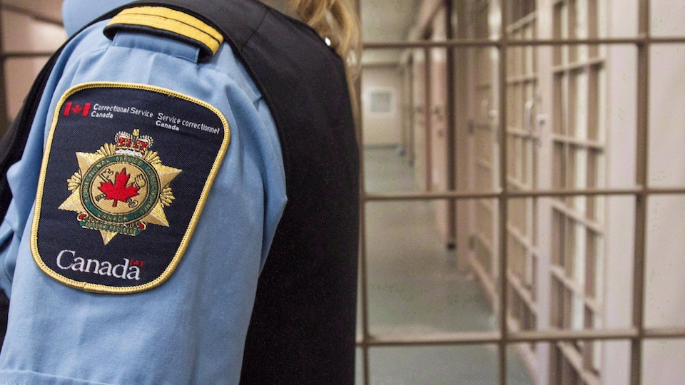 Un gardien de prison vu de profil, son visage à l'extérieur du cadre de la photo, avec son insigne bien visible sur le côté de son uniforme.