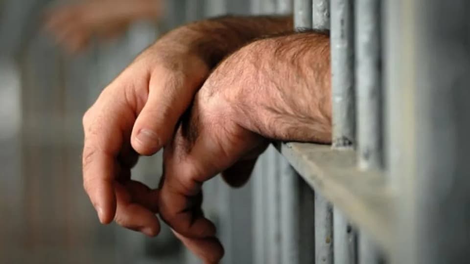 Les mains d'un détenu à l'extérieur des barreaux d'une cellule de prison.