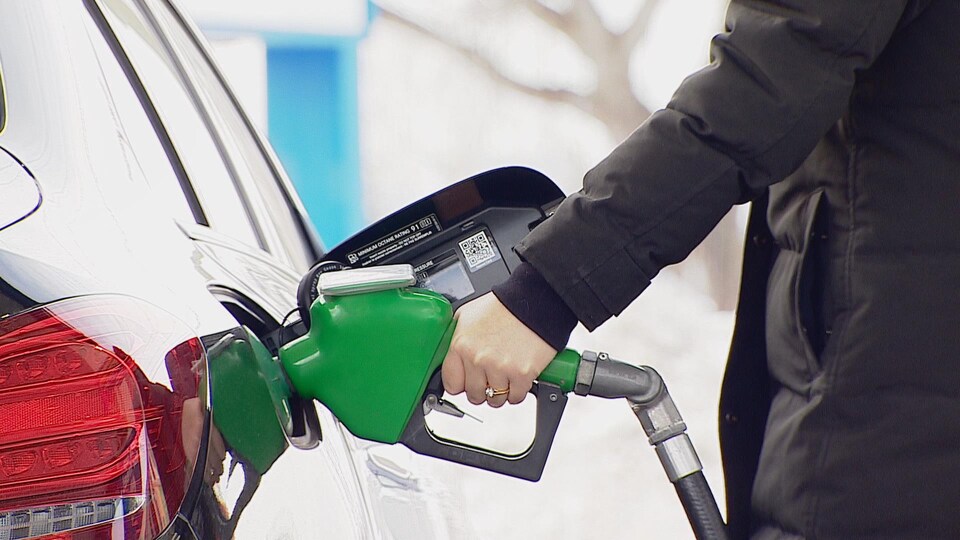 Une main de femme tient une pompe à essence verte. 