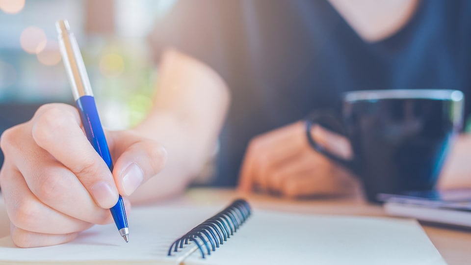 Une personne écrit avec un stylo dans un cahier.