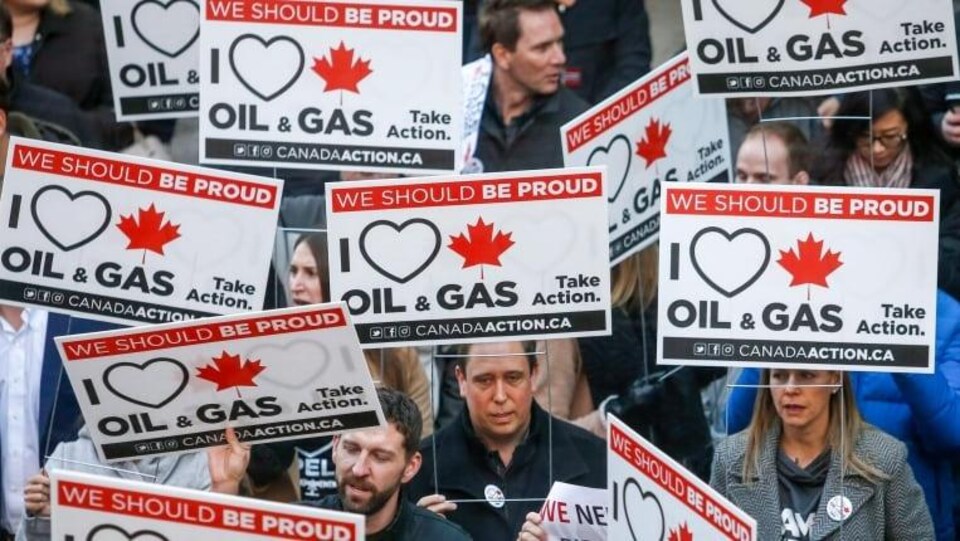 Une foule de manifestants brandit des pancartes indiquant en anglais: « we should be proud » et « I love oil and gas ».
