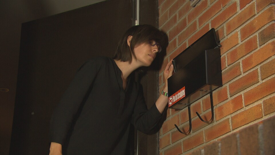Une jeune femme vérifie s'il y a du courrier dans sa boîte aux lettres, mais celle-ci est vide.