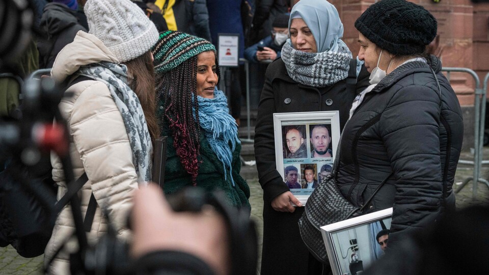 Quatre femmes discutent devant un tribunal. Deux d'entre elles tiennent un cadre avec des photos de leurs proches. 