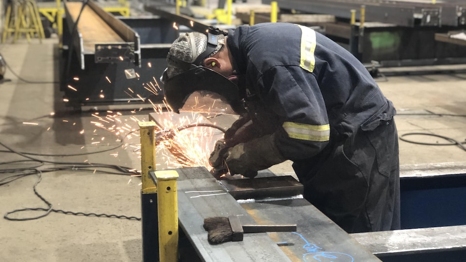 Un travailleur soude une pièce d'acier dans une usine.