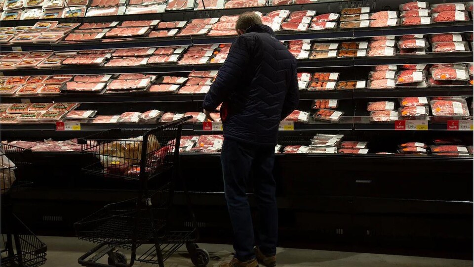 Un consommateur devant un étalage de viande dans une épicerie. 