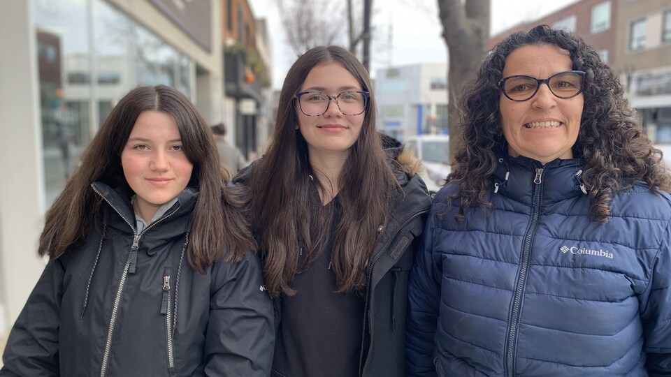 Deux étudiantes et leur enseignante posent pour la caméra à l'extérieur, manteaux sur le dos.