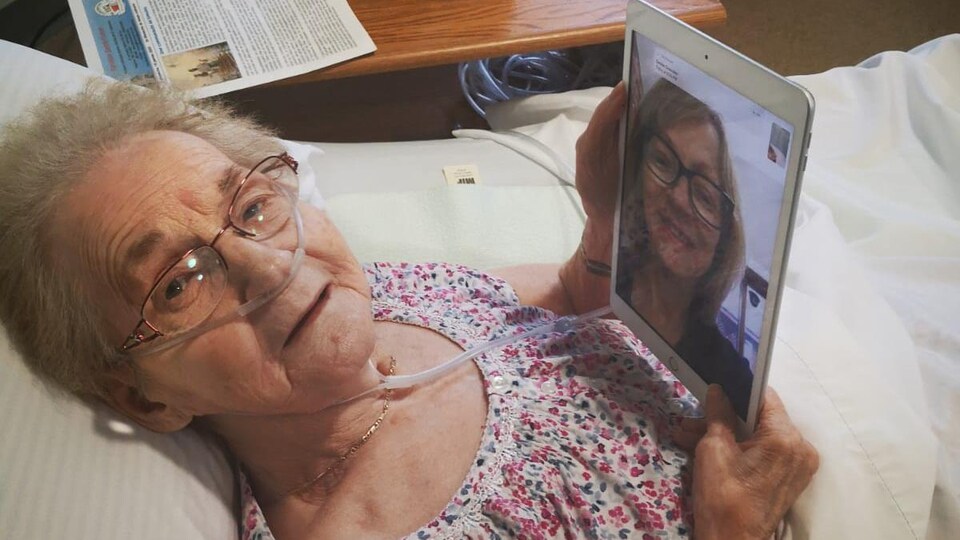 Une femme âgée dans son lit parle avec sa fille par l'entremise d'une tablette électronique.