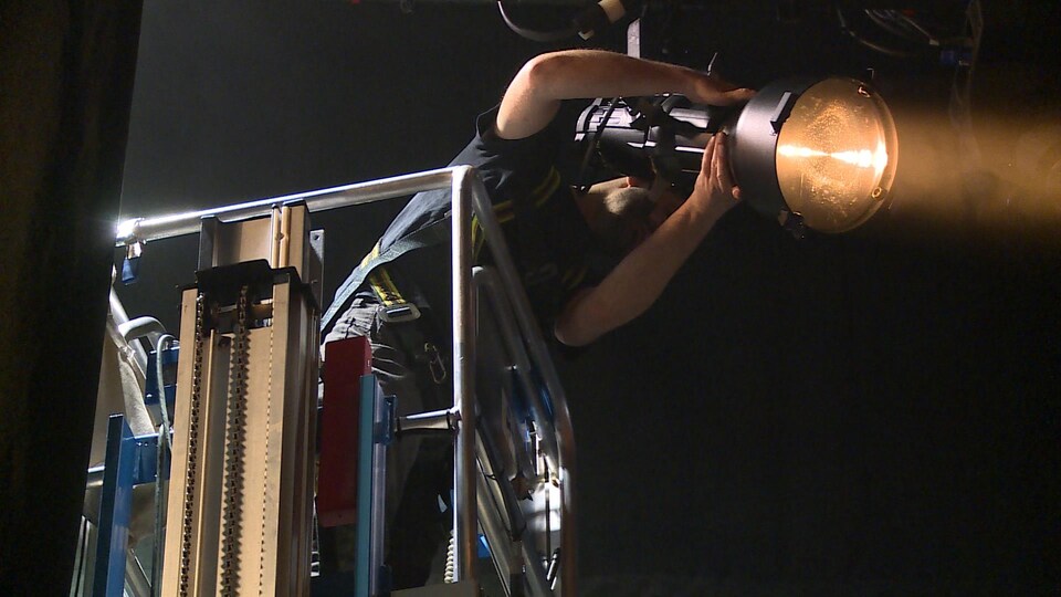 Dans une nacelle, un technicien de scène manie un projecteur de scène.