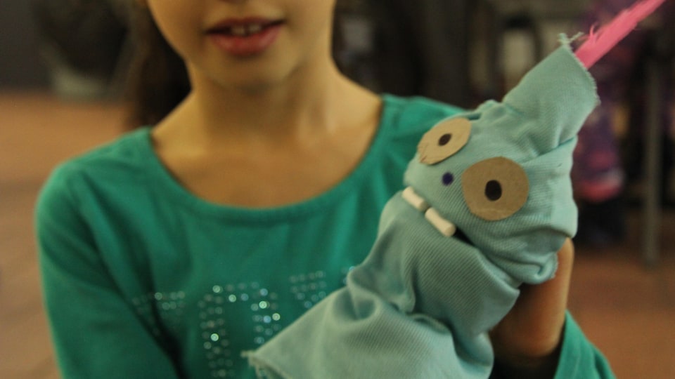Une enfant tient une marionnette verte fabriquée à la main.