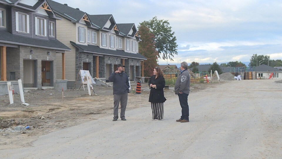 Trois personnes, debouts, dans un quartier de maisons en construction.