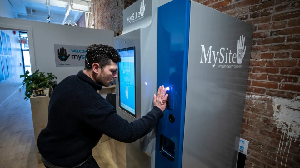 Devant une machine un peu plus grande qu'un guichet bancaire automatique, un homme pose sa main sur un scanneur situé à côté d'un écran d'information.