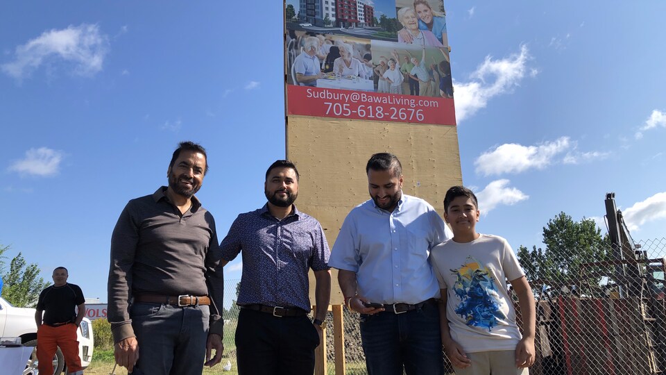 4 hommes posent devant une affiche annonçant une prochaine construction.