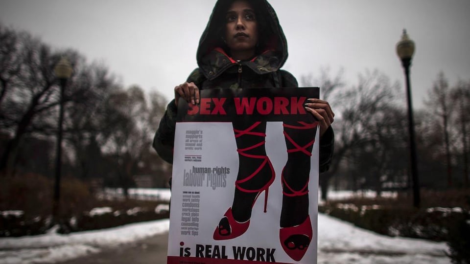 Une femme tient une affiche sur laquelle il est écrit, en anglais, que le travail sexuel est un vrai emploi, lors d'une manifestation devant la Cour suprême du Canada en 2013.