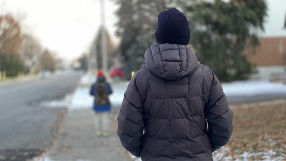 Une mère de dos regardant un garçon portant un sac à dos s'éloigner sur le trottoir
