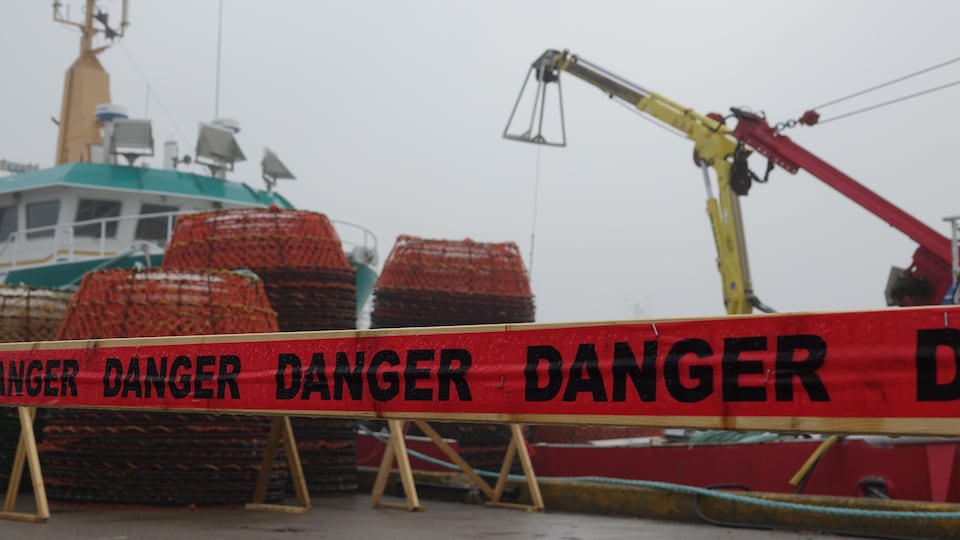 Une barrière sur laquelle le mot "danger" est répété plusieurs fois est installée devant un crabier amarré au quai. 