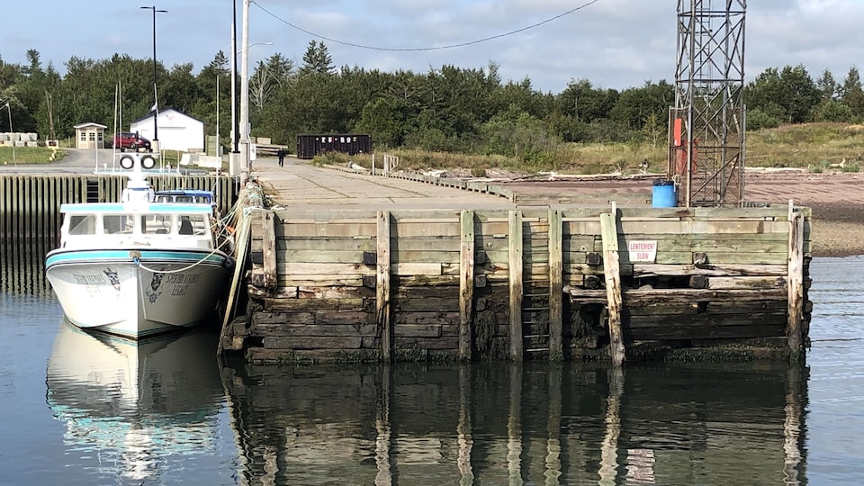Un bateau de pêche est amarré à un quai dont certains madriers ont dévié.