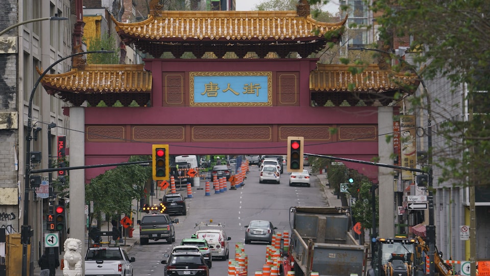 Vue d'ensemble des portes du quartier chinois de Montréal, sous lesquelles circulent beaucoup de voitures parmi des cônes de construction.