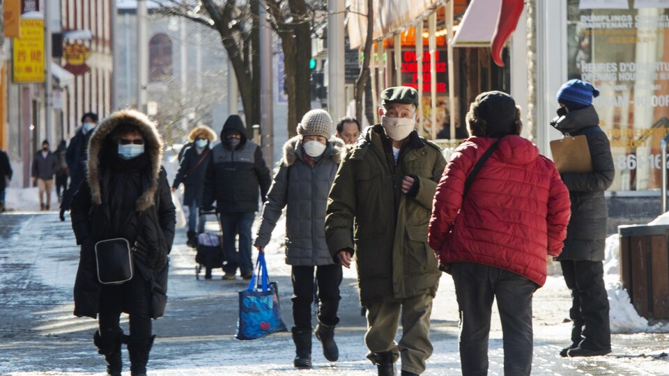 Des gens portant des masques se promènent dans une rue du Quartier chinois de Montréal.