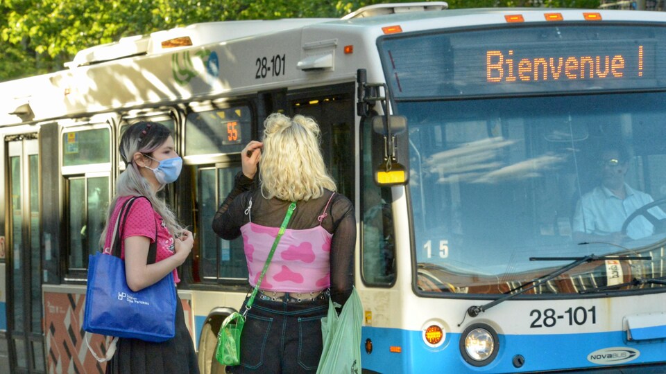 Deux femmes, dont une porte un masque, s'apprêtent à montre dans un bus.