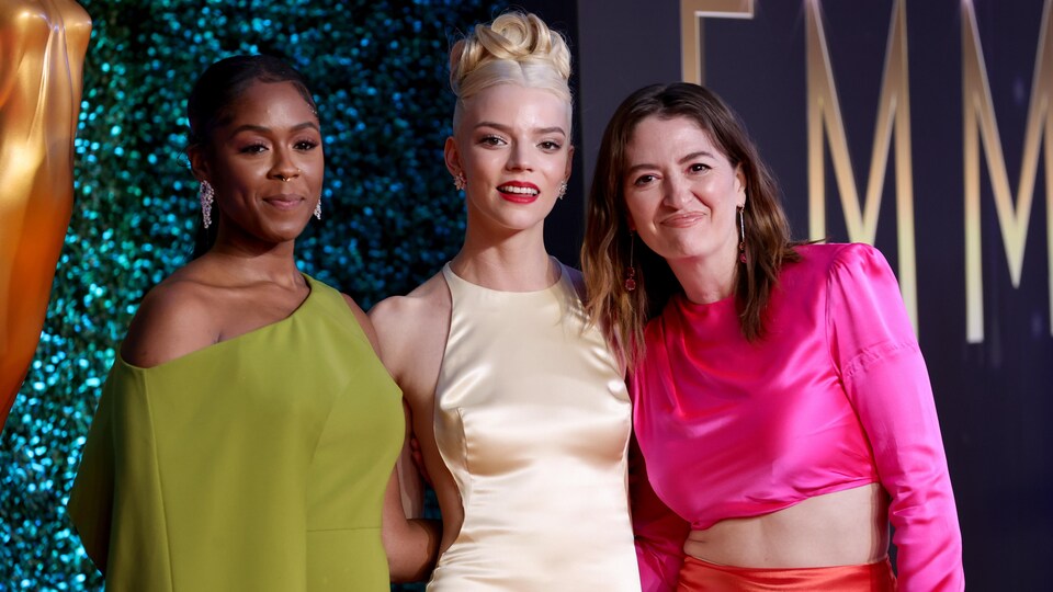 Trois femmes posent en robe de soirée devant un mur de paillettes bleu.