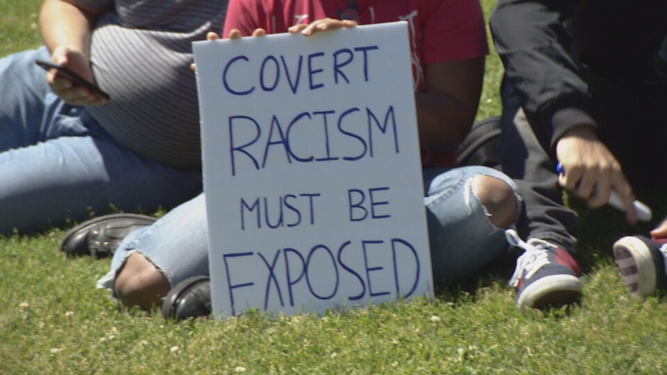Sur une pancarte une manifestante dénonce un racisme systémique dissimulé, qui doit "être dévoilé au grand jour".