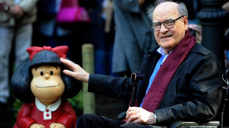 Quino, en fauteuil roulant, pose à côté de Mafalda.
