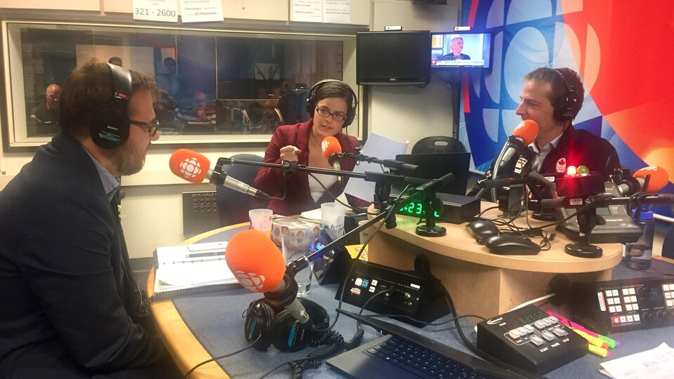 Catherine Doucet parle au micro en studio avec, de chaque côté, deux candidats.
