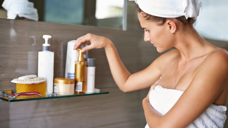 Une femme choisit un produit de beauté dans la salle de bain.