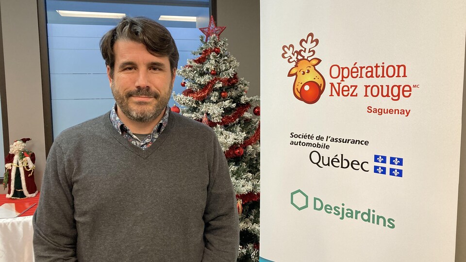 Le coordonnateur local de l'Opération Nez rouge de Saguenay, Patrick Lalande, se trouve devant un sapin de Noël.